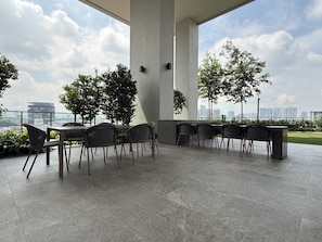 Un espace extérieur aménagé avec des tables et des chaises, entouré de grandes colonnes et de plantes en pot, offrant une vue sur le paysage urbain.