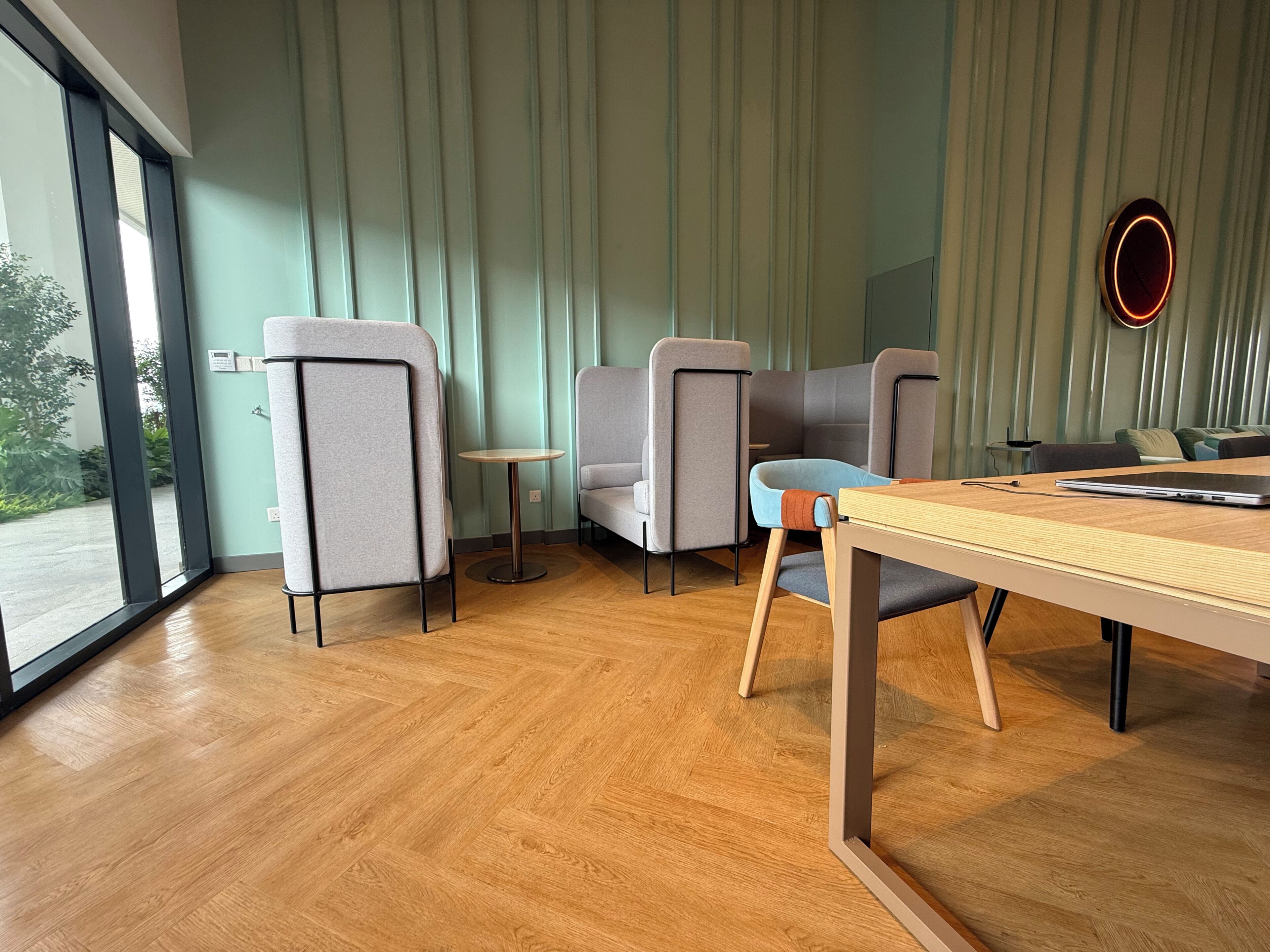 Un intérieur moderne avec un plancher en bois, des chaises grises et bleues, une petite table ronde et une grande fenêtre donnant sur l’extérieur.