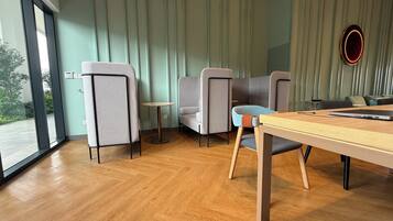 Un interior moderno con suelo de madera, sillas grises y azules, una pequeña mesa redonda y un ventanal con vistas al exterior.