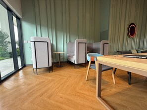 A modern interior with a wooden floor, grey and blue chairs, a small round table, and a large window offering a view outside. - Skyline Pudu by Manhattan (Kuala Lumpur)