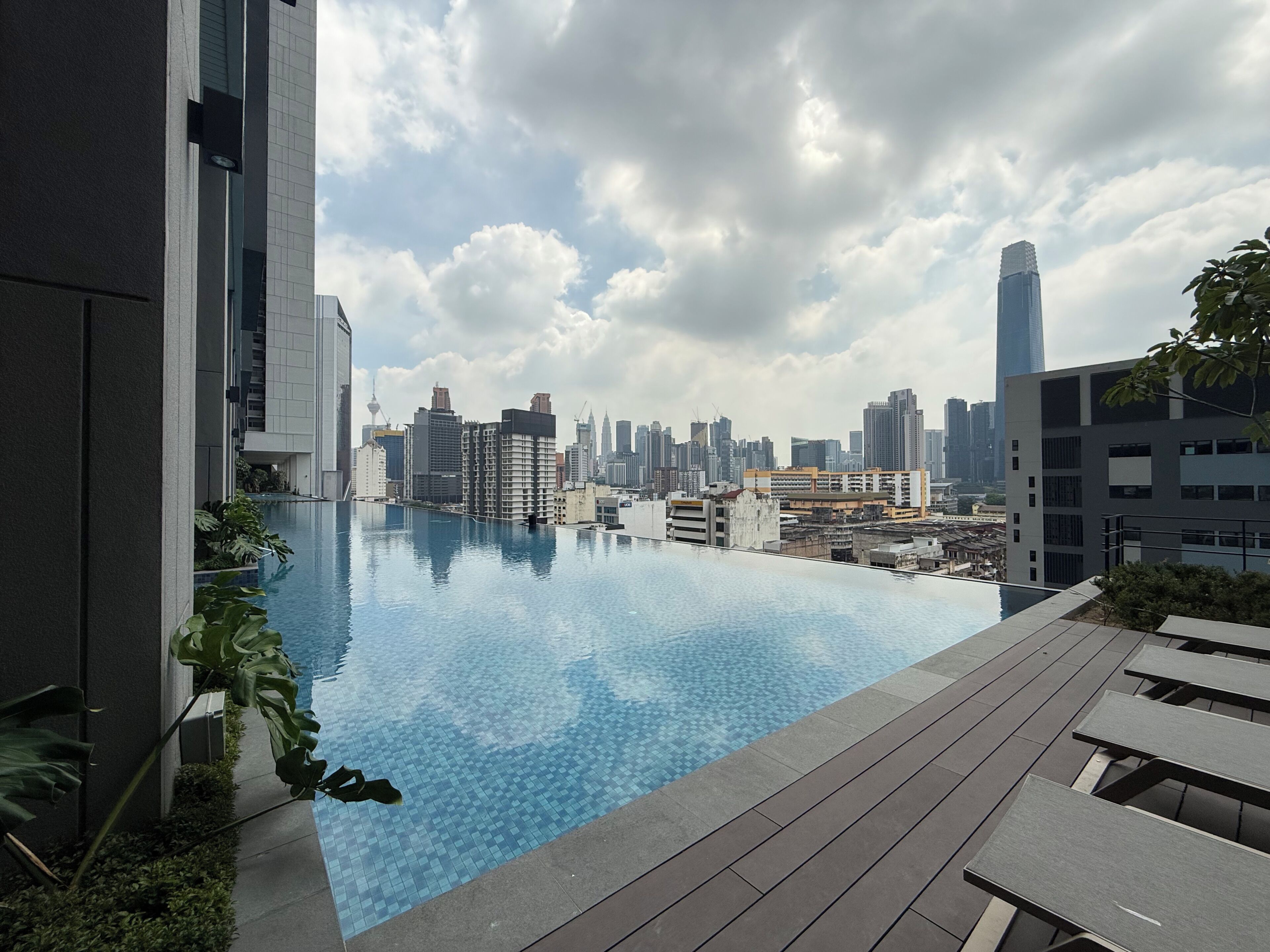 Piscina infinita en la azotea con vista al horizonte urbano, rodeada de edificios modernos y vegetación.
