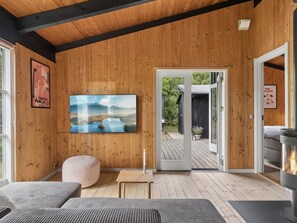 A wooden interior with a large painting, a cozy seating area, and a view through a glass door to an outdoor deck. - "Erich" - 500m from the sea by Interhome (Aakirkeby)