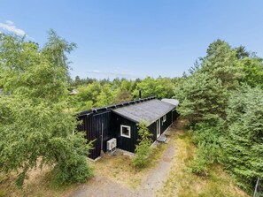 A small, single-story building with a dark exterior, surrounded by dense greenery and trees. - "Erich" - 500m from the sea by Interhome (Aakirkeby)