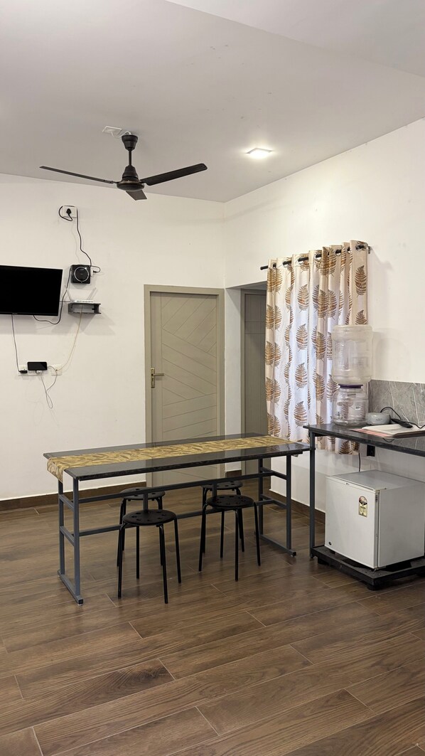 A room with a dining table, chairs, a ceiling fan, a water dispenser, and a refrigerator.
