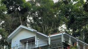 A two-story building with a flat roof, surrounded by dense greenery and trees.
