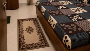 A bedroom with a bed, an air conditioning unit, a ceiling fan, a nightstand with a lamp, and a door. - Hotel GRG Bhavan Vrindavan (Mathura)