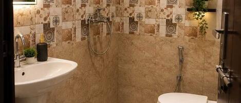 Une salle de bain comprenant un lavabo sur colonne, des toilettes, une douche avec un pommeau de douche amovible et un mur décoratif recouvert de carreaux.