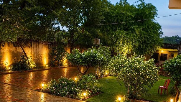 A courtyard with a paved walkway, a small garden area with plants and a tree, and a building in the background. - Hotel GRG Bhavan Vrindavan (Mathura)
