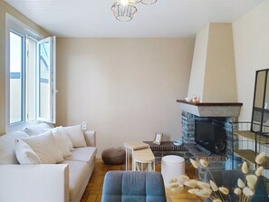 A living room with a sofa, a small table, a fireplace, and a window. - Riviera by Interhome (Agon-Coutainville)