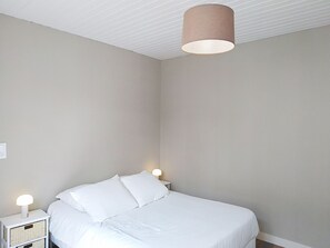 A bedroom with a bed, bedside lamps, and a ceiling light fixture. - Riviera by Interhome (Agon-Coutainville)