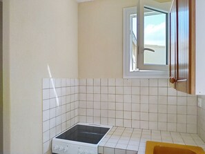 Uma cozinha pequena com azulejos brancos, um fogão e uma janela.