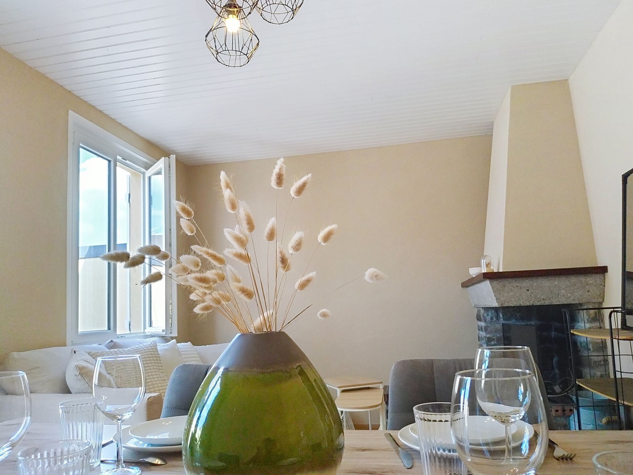 Un comedor con una mesa dispuesta para dos, un florero con plumas de pampa seca y una chimenea.