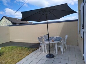 Um pátio com mesa redonda e cadeiras, um guarda-sol preto e piso de azulejos.