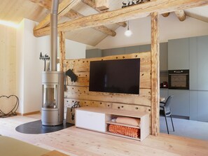 Ein modernes Wohnzimmer mit großem Flachbildfernseher an einer Holzwand, einem eingebauten Kamin und einem Essbereich mit einem Stuhl.