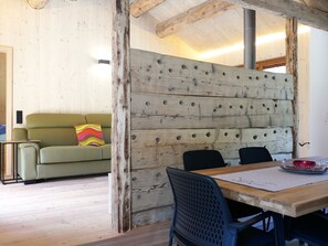 Ein Zimmer mit Holzwand, einem grünen Sofa, einem Esstisch mit Stühlen und Holzboden.