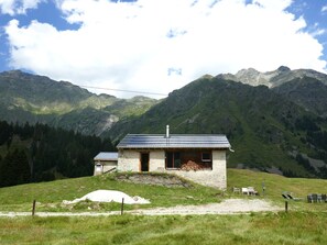 Eine Berglodge mit Steinaußenwand, geneigtem Dach und Blick auf die umliegenden Berge.