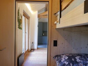 A narrow hallway leading to a room with a bunk bed, wooden flooring, and a door with a decorative plant. - Nido delle Alpi by Interhome (San  Bernardino)