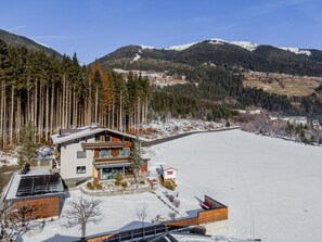 A modern two-story building with a ski lift, surrounded by snow-covered ground and dense forest. - Spacious living with alpine charm and balcony (Neukirchen am Großvenediger)