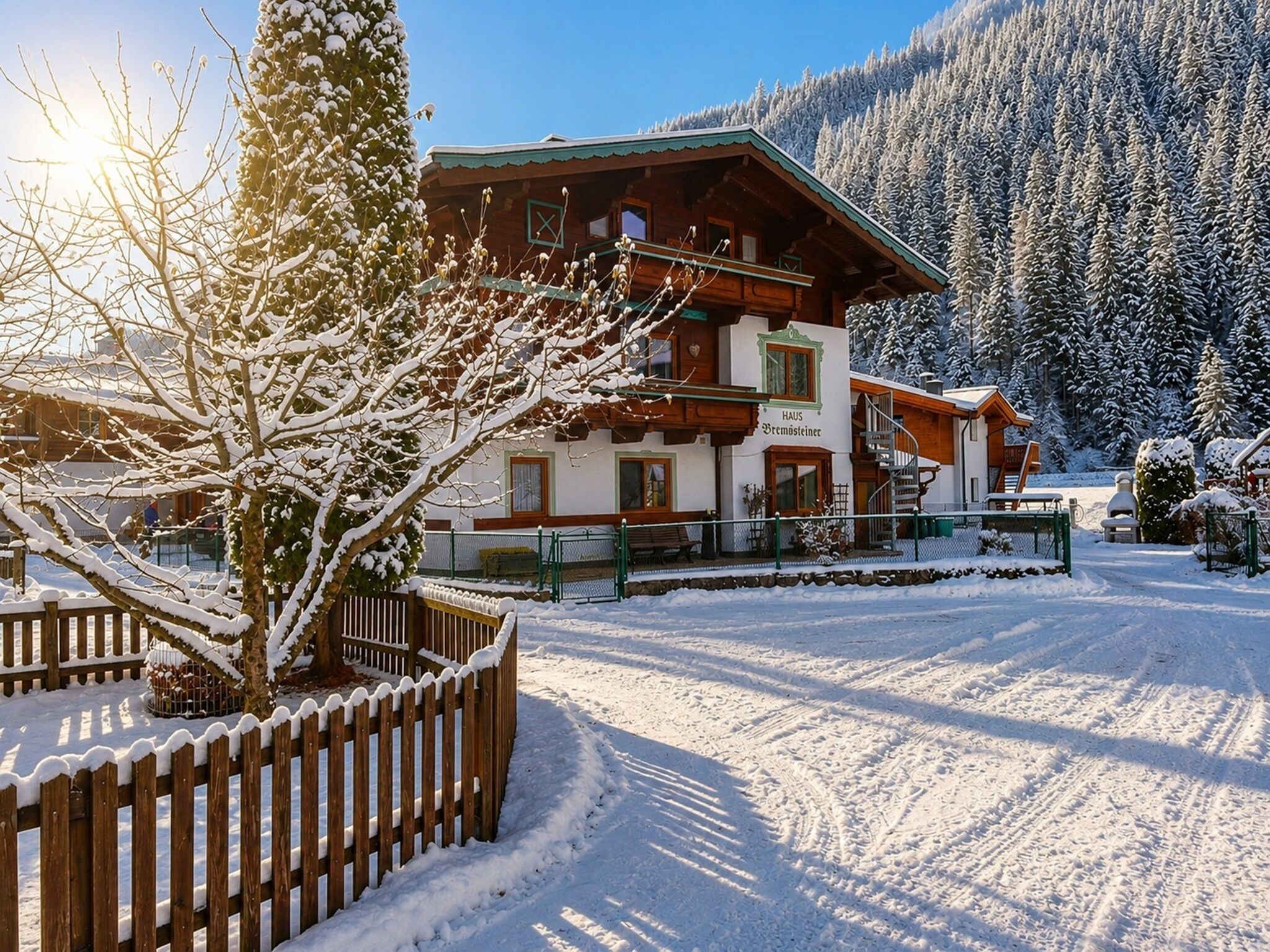 Eine Holzhütte mit Balkon, umgeben von schneebedeckten Bäumen und wolkenlosem Himmel.