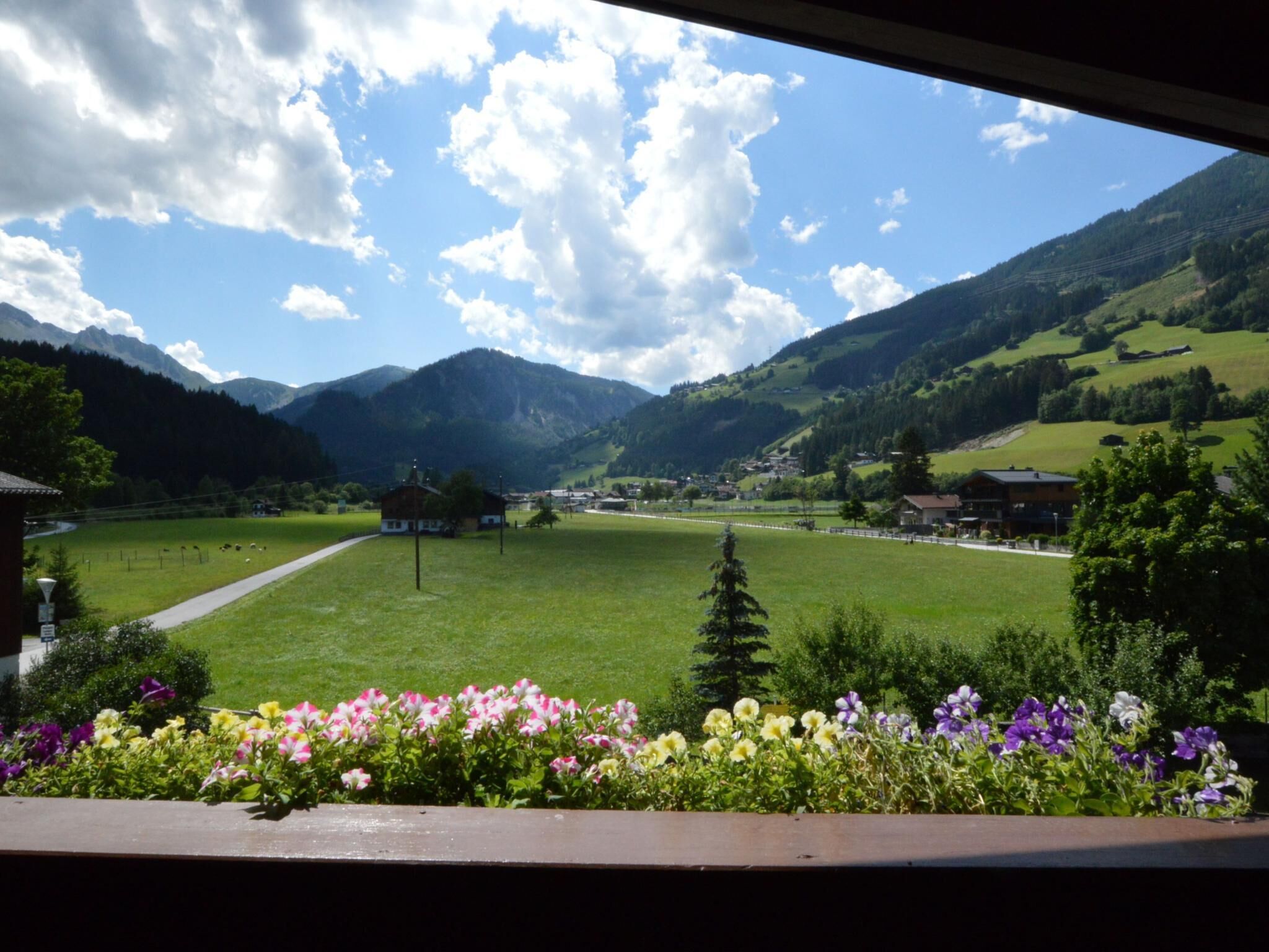 A view of a mountain landscape with a clear sky, a green field, and a building in the distance.