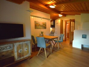 Ein Essbereich mit Holztisch und Stühlen, einem an der Wand montierten Fernseher und einem Gemälde über dem Tisch.