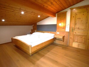 Ein Schlafzimmer mit Holzboden, einem Bett, einem Nachttisch, einer Kommode und einer Wandleuchte.