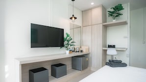 A modern bedroom with a flat-screen TV, built-in storage, a bedside table, a lamp, and a potted plant.