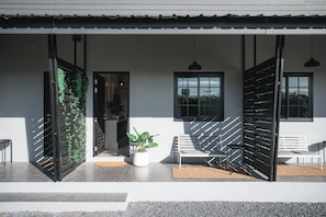 A modern building with a covered outdoor seating area, a potted plant, and a bench.
