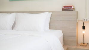 Una cama bien hecha con sábanas blancas, cabecera de madera y mesita de noche con lámpara.
