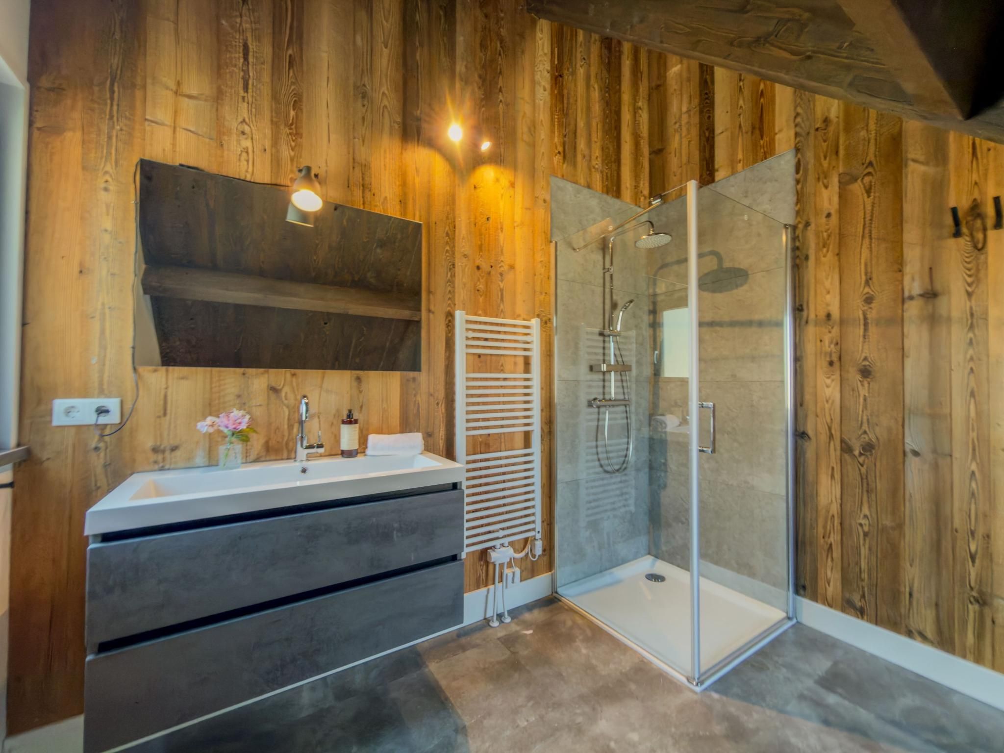 Une salle de bain avec un lambris en bois, une cabine de douche en verre, un lavabo blanc et un porte-serviettes.