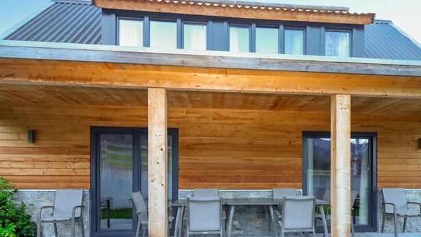Ein überdachter Patio-Bereich mit Tisch und Stühlen, eine Steinmauer und ein Holzdeck.