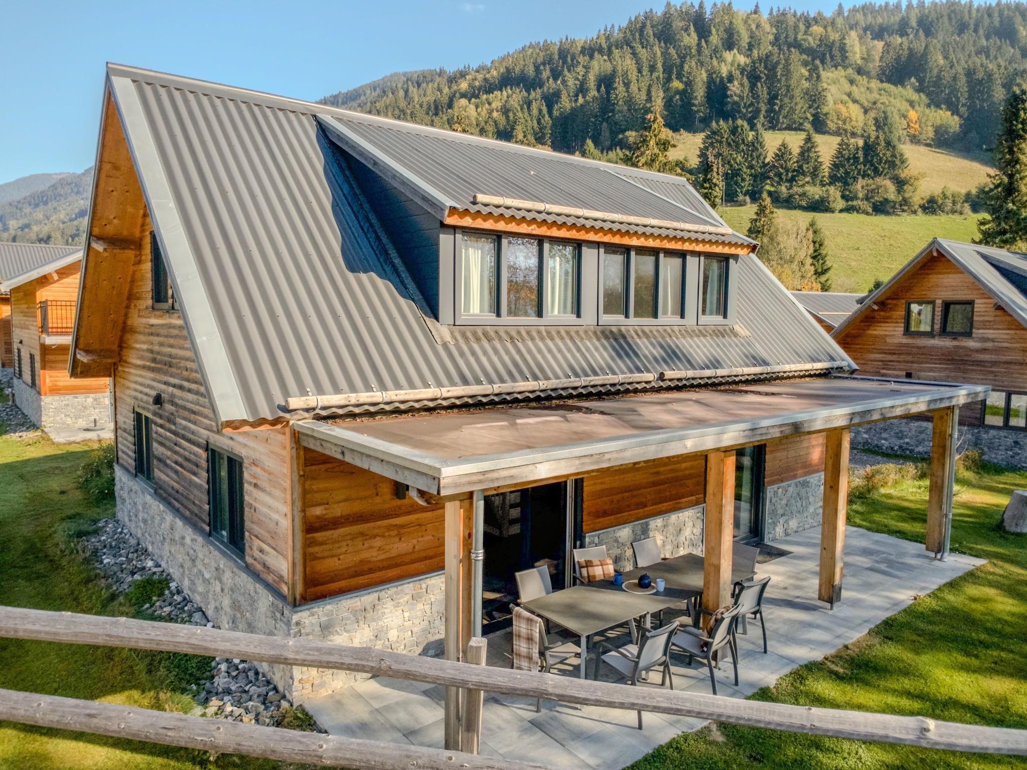 A modern cabin with a sloped metal roof, wooden exterior, and a covered patio with outdoor furniture.