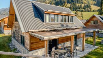 A modern cabin with a sloped metal roof, wooden exterior, and a covered patio with outdoor furniture.