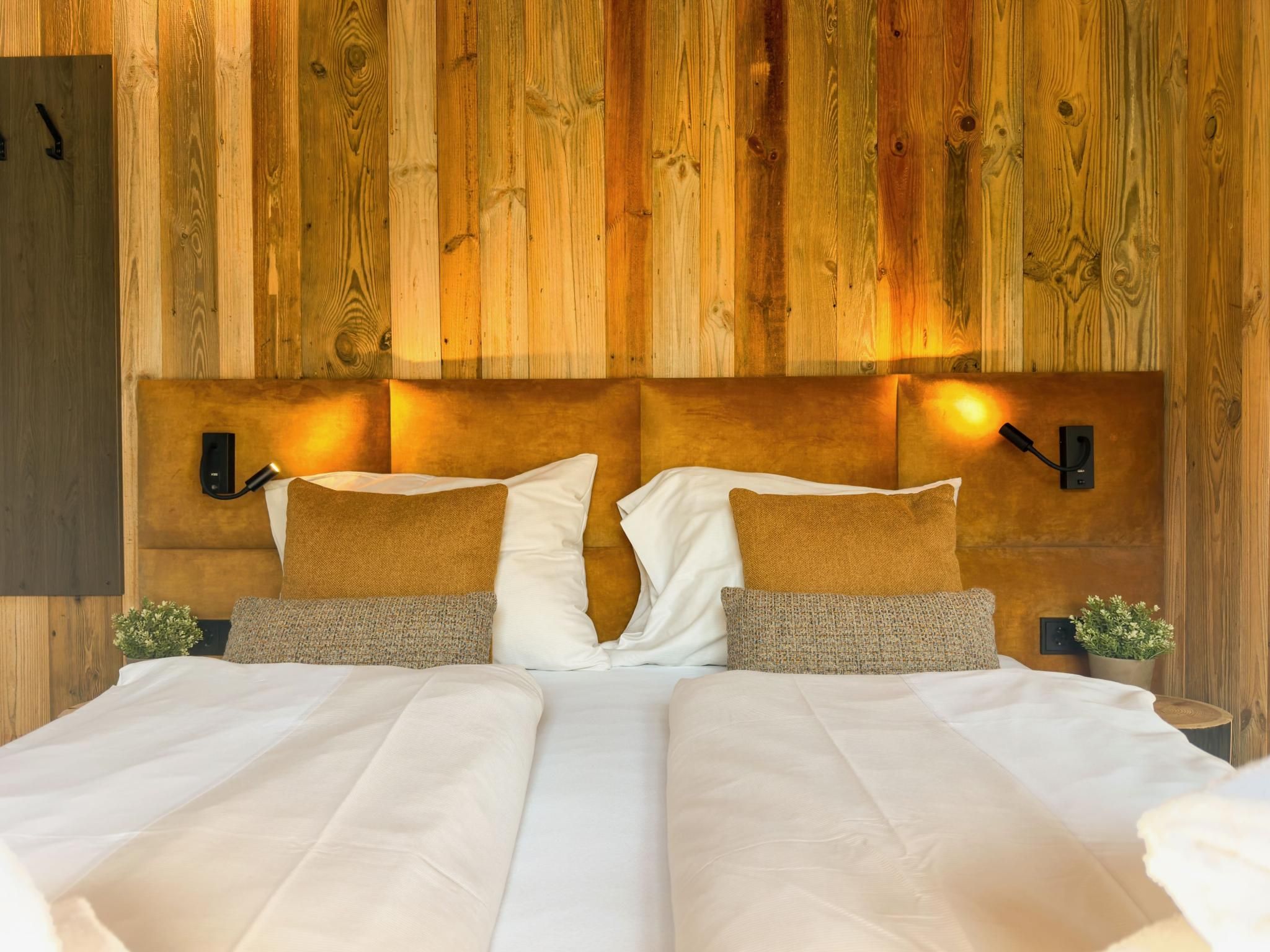 A double bed with white linens, two pillows, and a wooden headboard with wall-mounted lights.