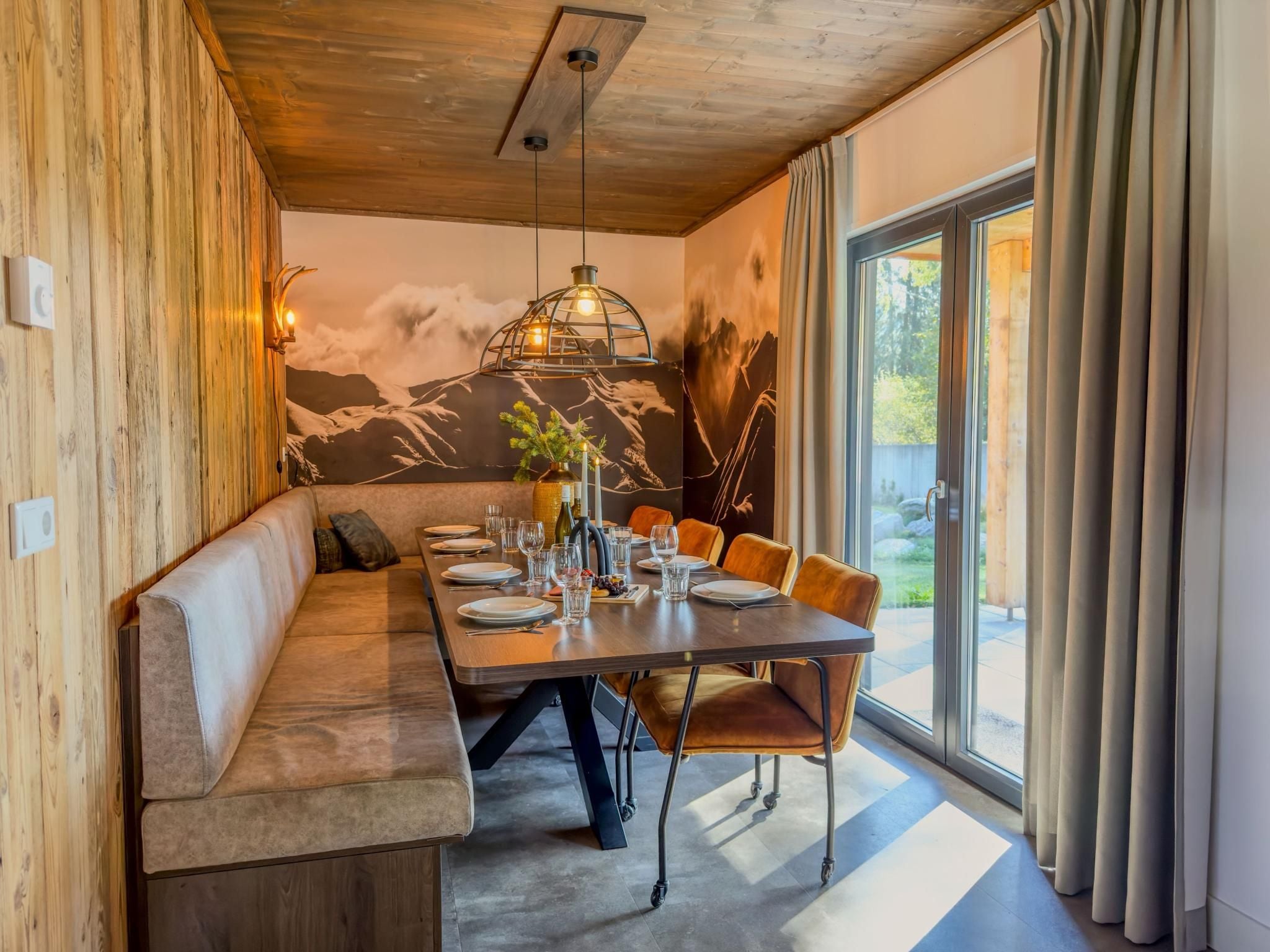 Un espace repas moderne avec un banc en bois, une table à manger dressée pour six personnes et une fresque représentant une montagne sur le mur.
