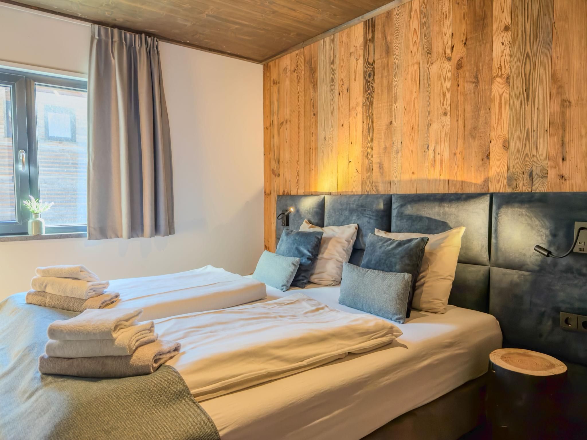 Une chambre à coucher moderne avec une tête de lit en bois, deux lits et une table de chevet avec une lampe.