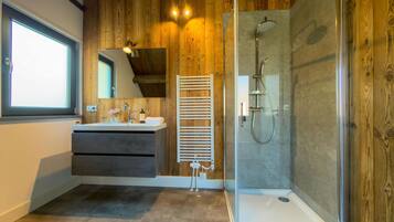 A modern bathroom with a glass-enclosed shower, wooden paneling, a vanity with a mirror, and a window.
