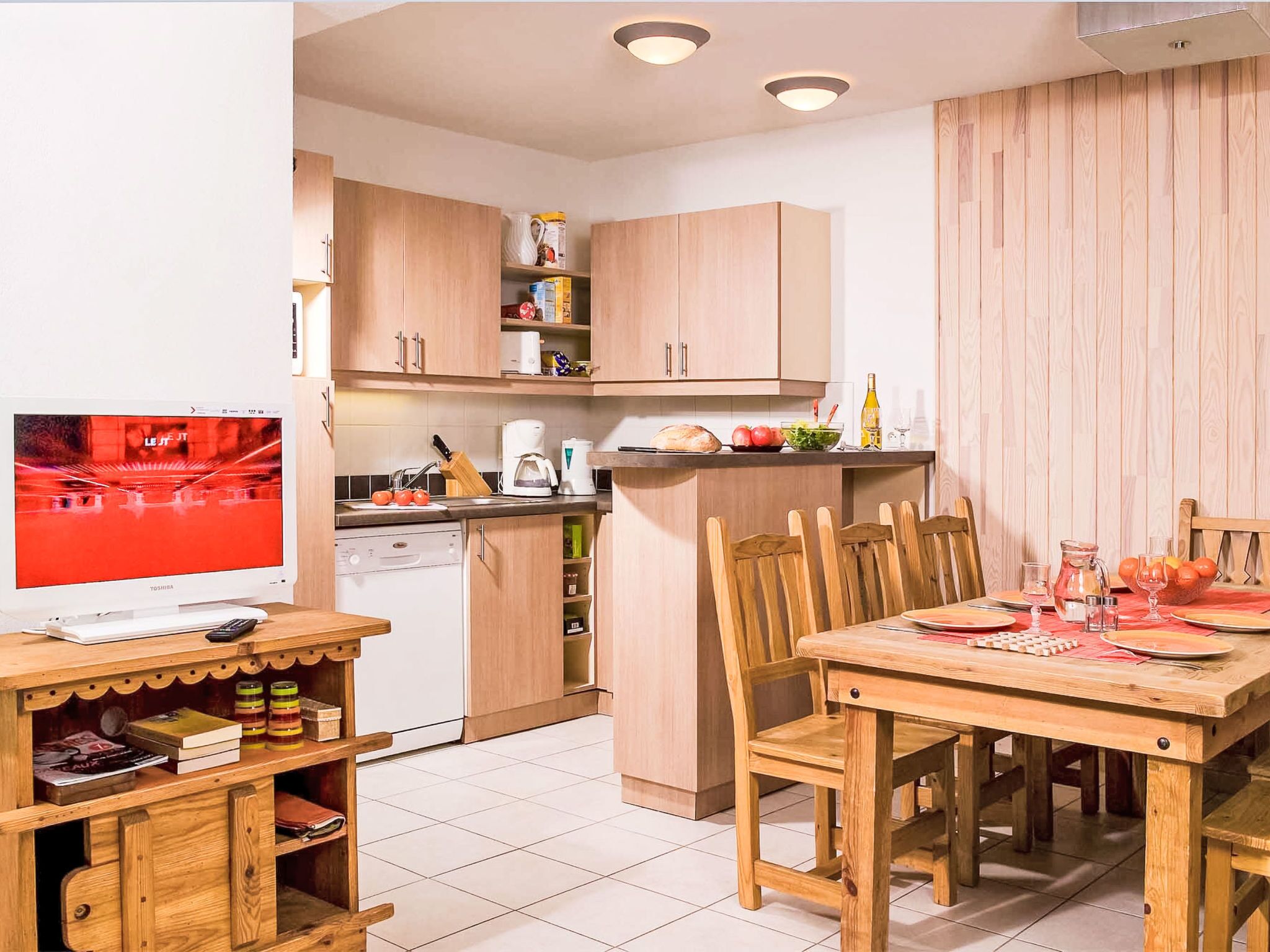 A compact kitchen with wooden cabinets, a dining table, and a TV.