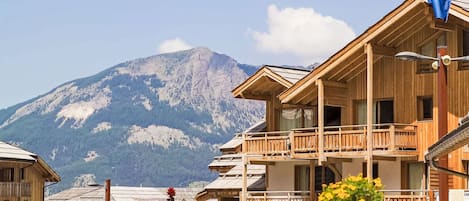 A wooden chalet with balconies, a mountain backdrop, and a clear sky.