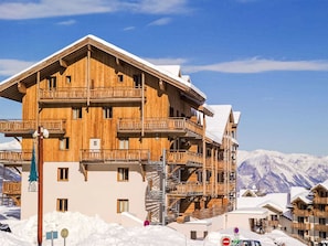Eine mehrstöckige Holzhütte mit Balkonen vor einer verschneiten Berglandschaft.