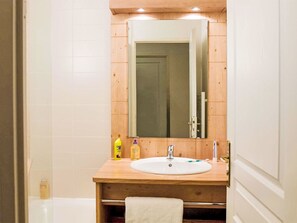 Ein Badezimmer mit einem Holzkosmetikschrank, einem Waschbecken, einem Spiegel und einem Handtuchhalter.