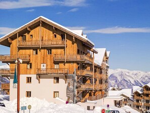 Eine mehrstöckige Holzhütte mit Balkonen vor einer verschneiten Berglandschaft.
