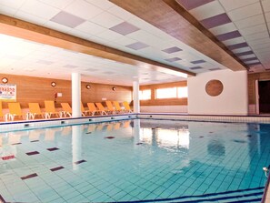 Ein Hallenbad mit gefliesten Wänden und Decke, Holzvertäfelung und einem gut einsehbaren Poolbereich.