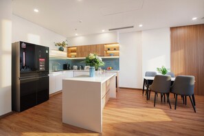 A modern kitchen with a central island, wooden cabinets, and a dining area with chairs. - VENTURA by BRIO (Da Nang)