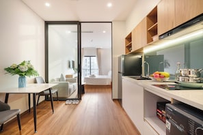 A compact kitchen with modern appliances, a dining area with a table and chairs, and a view into a bedroom. - VENTURA by BRIO (Da Nang)
