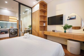 Habitación de hotel con cama, escritorio, televisor, espejo, planta y basurero.