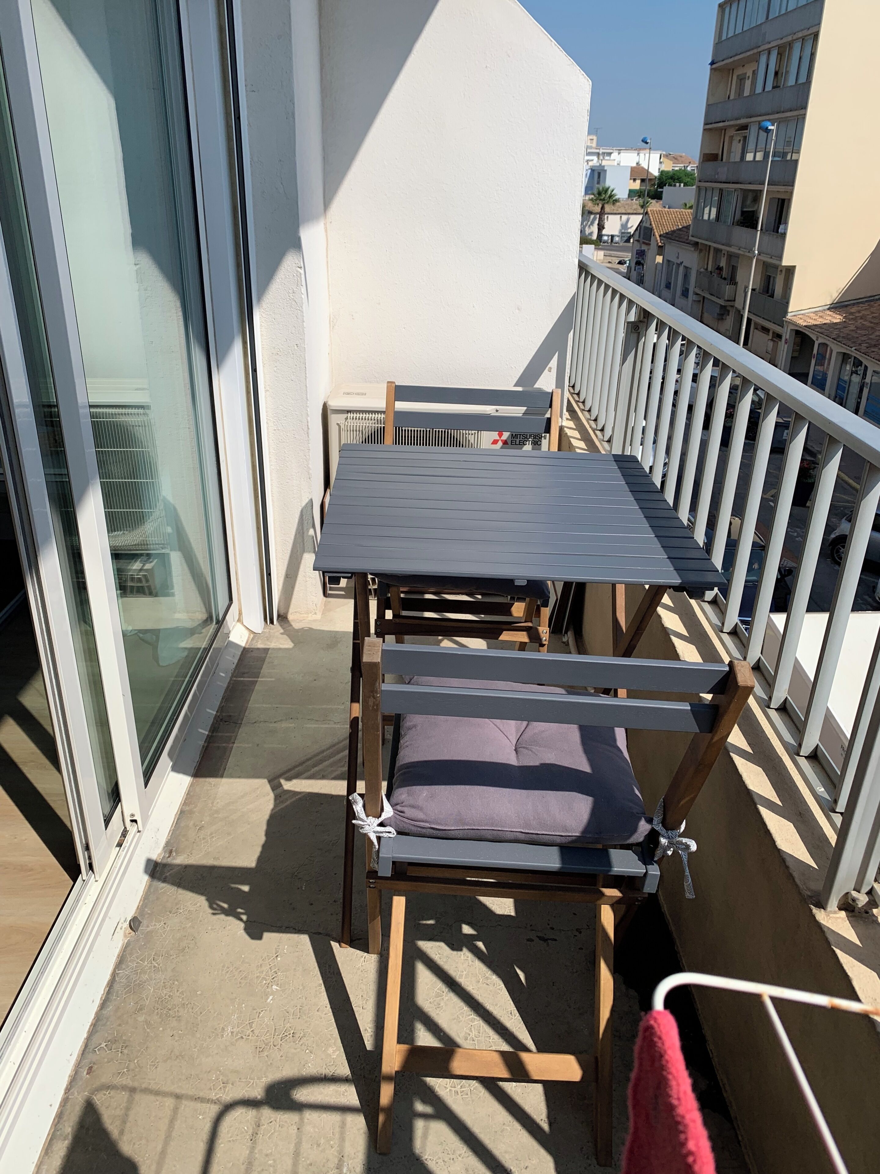 A balcony with a table and chairs, a white railing, and a view of buildings.