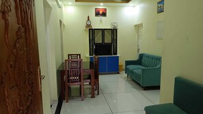 A living room with a sofa, a dining table with chairs, a TV, and a clock on the wall.