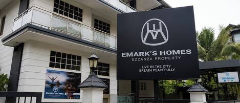 Un edificio de varios pisos con un letrero que indica Emark's Homes Ezzanza Property, con balcones y una entrada protegida por una reja.