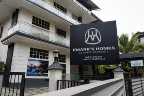 Un edificio de varios pisos con un letrero que indica Emark's Homes Ezzanza Property, con balcones y una entrada protegida por una reja.